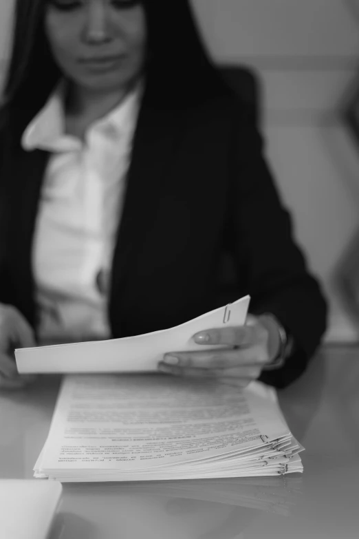 a woman sitting at a table reading a piece of paper, a black and white photo, by Romain brook, pexels, subject detail: wearing a suit, holding court, stacked image, uploaded