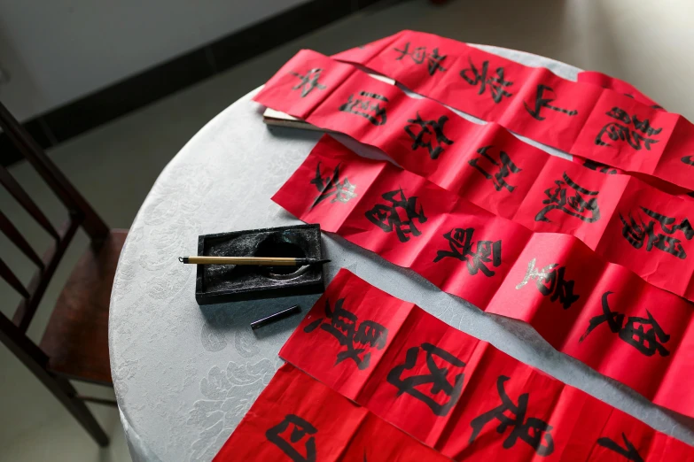 a table topped with lots of red paper and chopsticks, a silk screen, inspired by Cao Buxing, unsplash, gutai group, red banners, estrange calligraphy, high-quality photo, cloth accessories