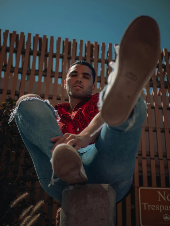 a man sitting on top of a wooden post, an album cover, by Adam Dario Keel, pexels contest winner, red boots, lean man with light tan skin, ( ( ( wearing jeans ) ) ), non-binary