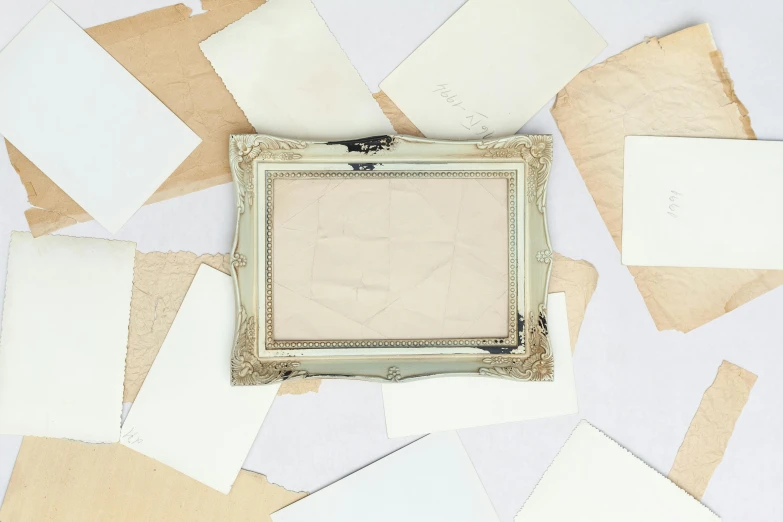 a picture frame sitting on top of a pile of papers, inspired by Rachel Whiteread, unsplash contest winner, vintage postcard, shattered abstractions, silver，ivory, square pictureframes