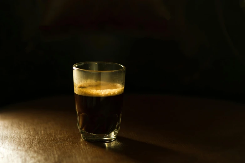 a glass of coffee sitting on top of a wooden table, unsplash, australian tonalism, medium format, dark brown, small, dark angel of coffee