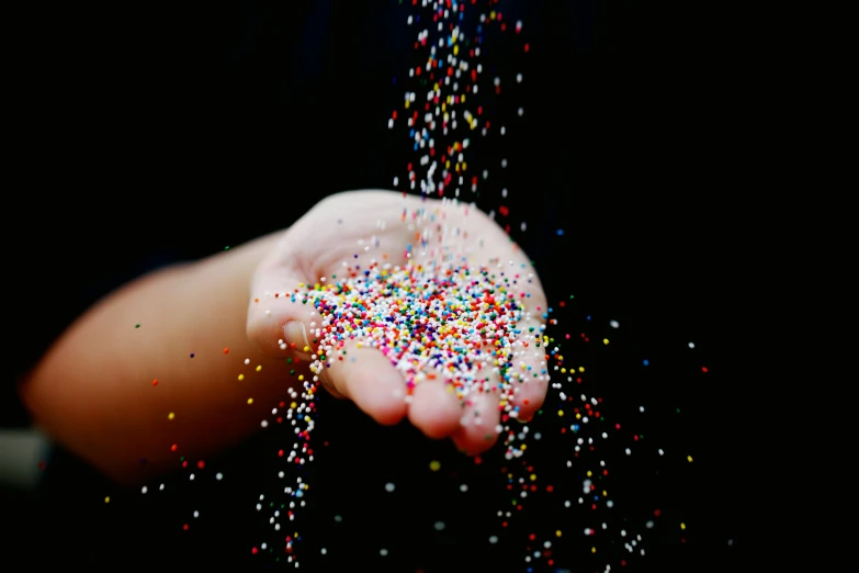 a person holding a handful of sprinkles in their hands, by Jan Rustem, pexels, pointillism, with a black background, gif, candy decorations, splash image
