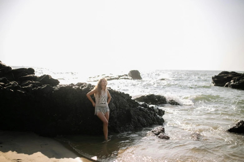 a woman standing on a rock in the ocean, a picture, unsplash, medium format, annasophia robb, southern california, slightly sunny