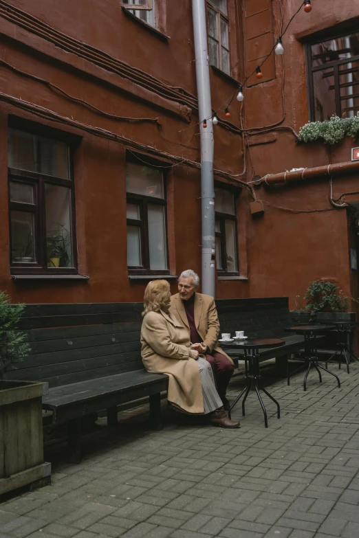 a couple of people that are sitting on a bench, a photo, pexels contest winner, socialist realism, courtyard, cafe, atmospheric warm colorgrade, russia