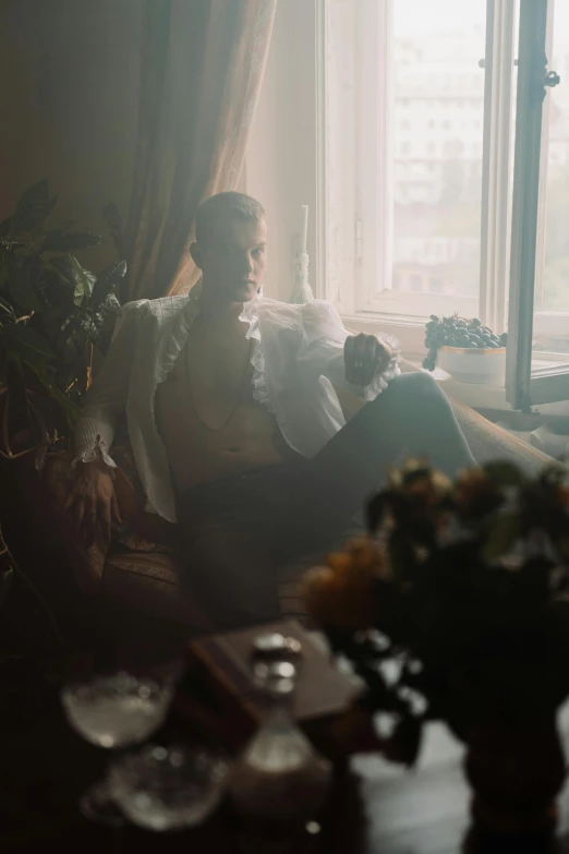 a woman sitting on a couch in front of a window, an album cover, inspired by Elsa Bleda, romanticism, handsome man, alexey egorov, grainy movie still, smoking