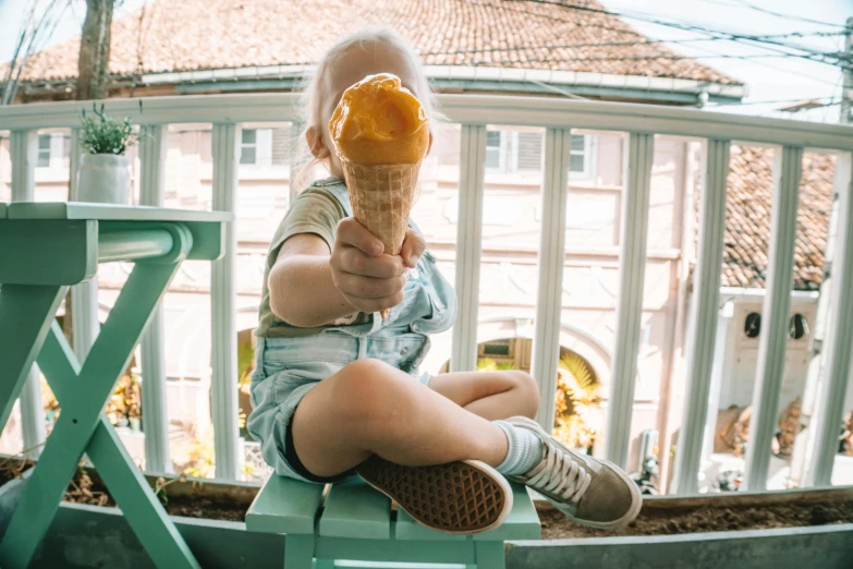 a child sitting on a chair eating an ice cream cone, by Emma Andijewska, pexels contest winner, balcony, looking up at the camera, 15081959 21121991 01012000 4k, caramel