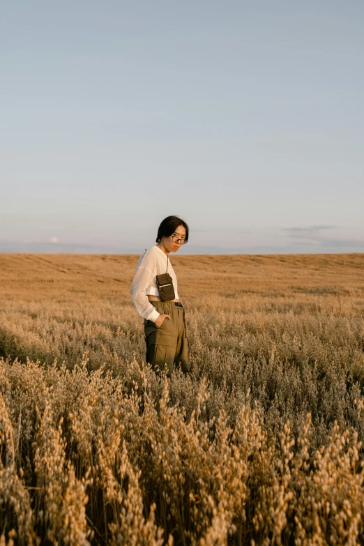 a man standing in a field of tall grass, an album cover, inspired by Russell Drysdale, trending on unsplash, japanese countryside, wearing overalls, a lonely woman, evening light