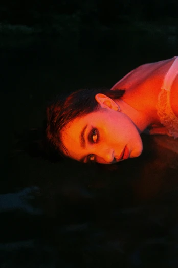 a woman laying on top of a body of water, an album cover, inspired by Elsa Bleda, pexels contest winner, intense watery glowing red eyes, she looks like a mix of grimes, shot at dark with studio lights, looking partly to the left