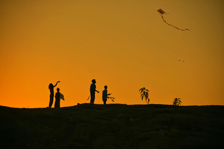 a group of people standing on top of a hill flying kites, a picture, by Max Dauthendey, pexels contest winner, silhouette!!!, lonely family, shot on sony a 7, orange skies