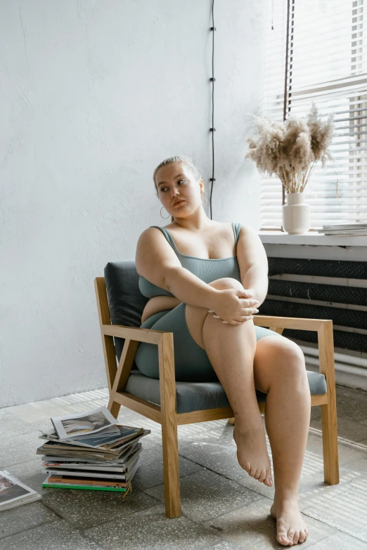 a woman sitting in a chair next to a window, pexels contest winner, thick body, is wearing a swimsuit, extremely uncomfortable, non binary model