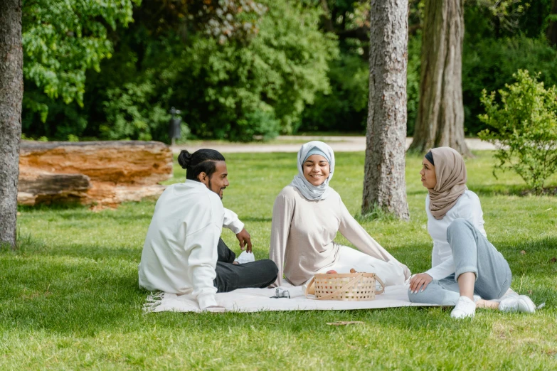 a group of people sitting on top of a grass covered field, white hijab, having a picnic, botanic garden, brown