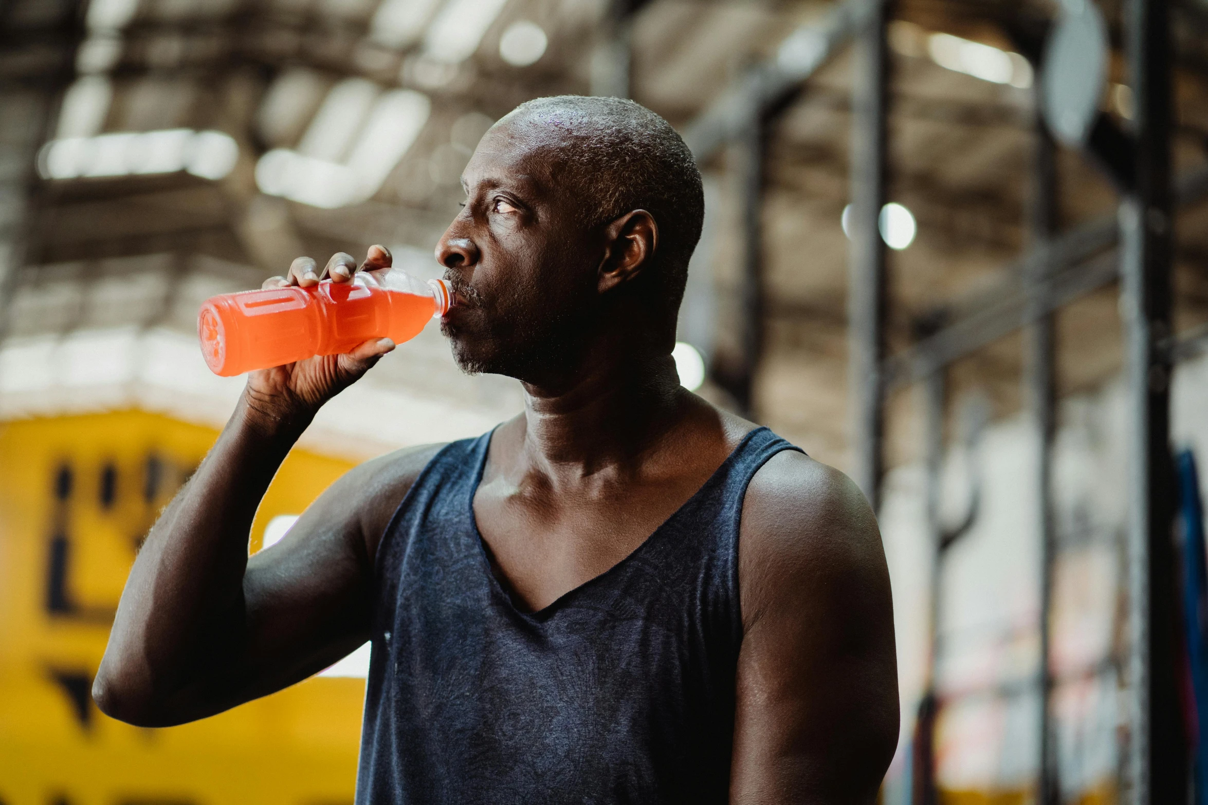 a man drinking an orange drink in a gym, pexels contest winner, man is with black skin, lachlan bailey, brightly coloured, in a warehouse