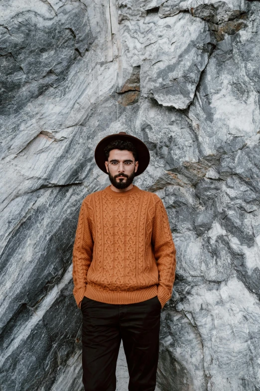 a man standing in front of a rock wall, an album cover, inspired by Lubin Baugin, pexels contest winner, he is wearing a brown sweater, braided beard, 5 0 0 px models, wearing wool hat