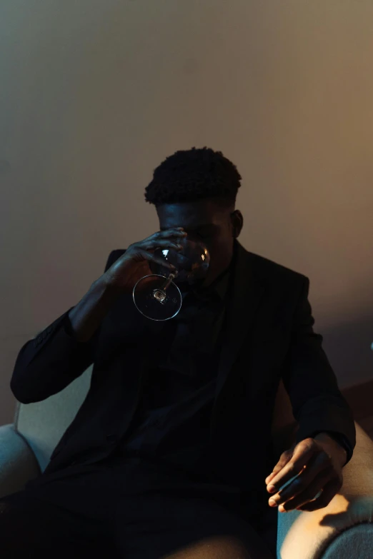 a man sitting on a couch drinking from a wine glass, an album cover, by Stokely Webster, pexels contest winner, dark skinned, grainy movie still, dark suit, college