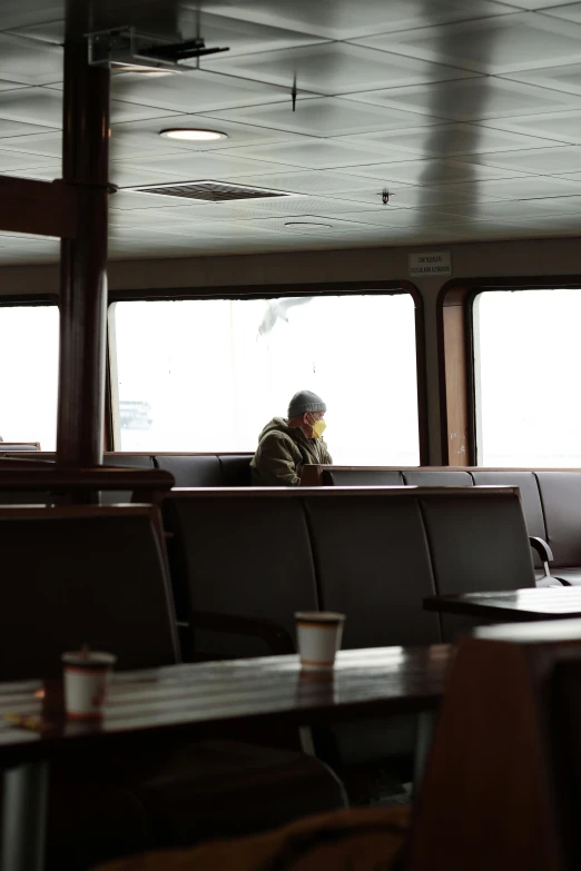 a man sitting at a table in a restaurant, inside large window of ship, low visibility, waiting room, fjord