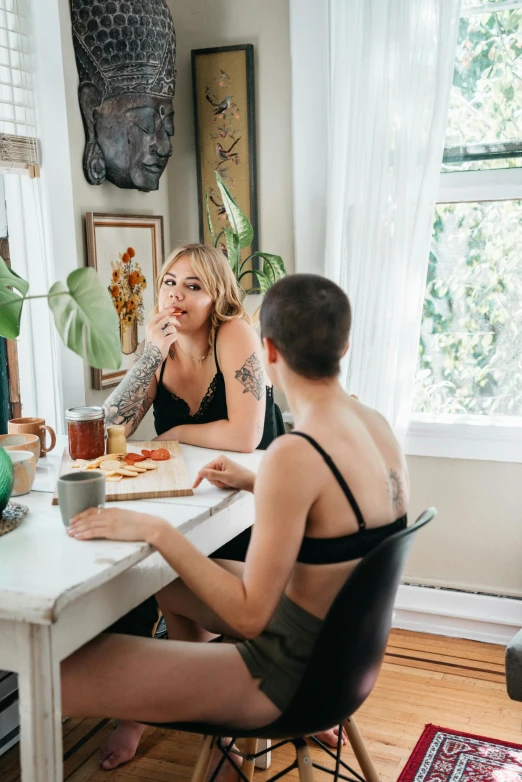 a couple of people that are sitting at a table, by Jessie Alexandra Dick, trending on pexels, queer woman, bralette, at home, tattooed