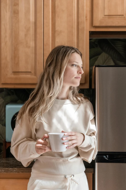 a woman standing in a kitchen holding a cup, a portrait, trending on unsplash, calmly conversing 8k, caucasian, aurora aksnes, profile image