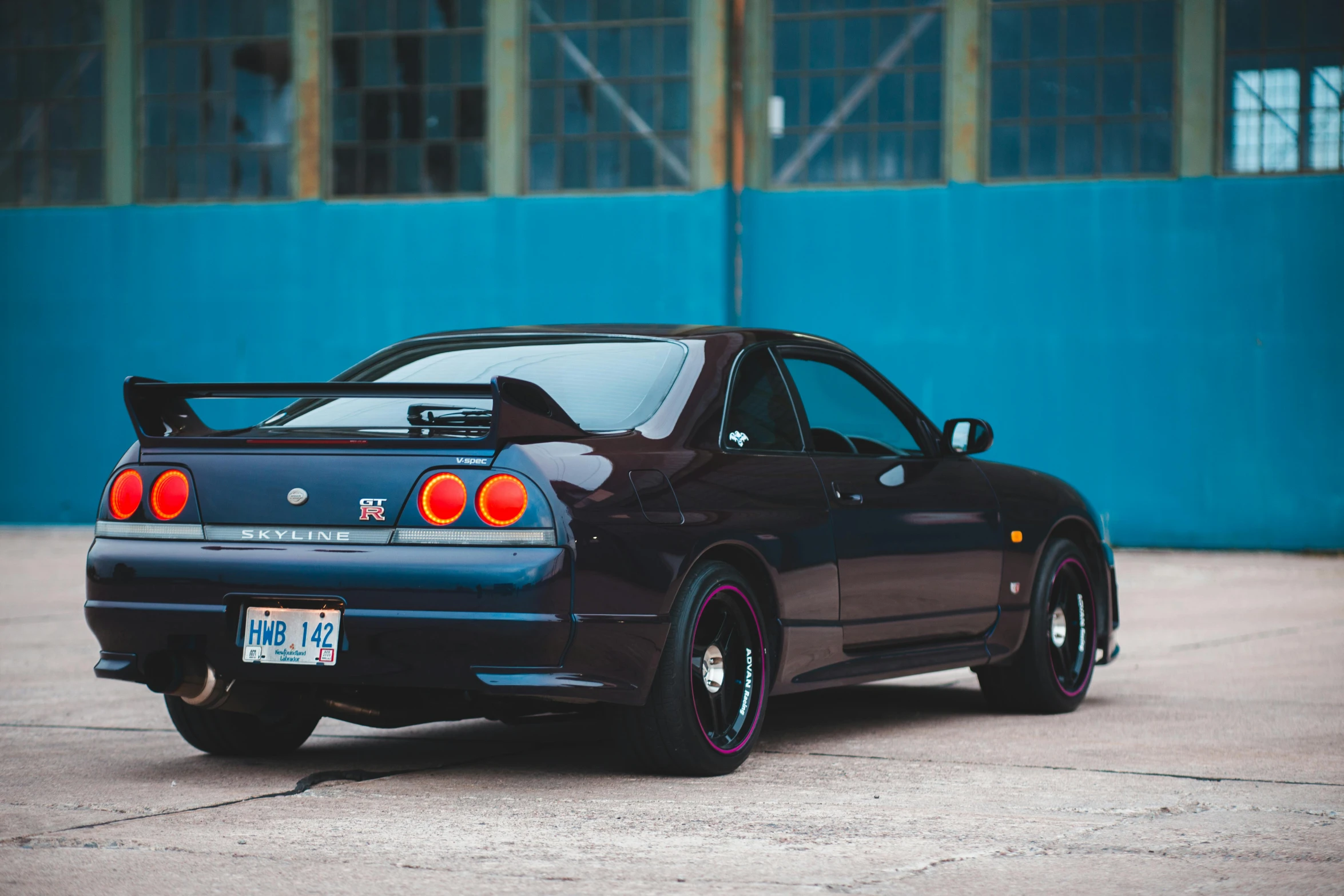 a black car parked in front of a blue wall, unsplash, mingei, in a modified nissan skyline r34, profile image, brown tail, in front of a garage