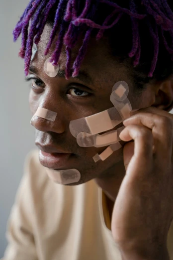 a man with purple dreadlocks talking on a cell phone, an album cover, trending on pexels, afrofuturism, covered in bandages, cute bandaid on nose!!, battle scars across body, a young man