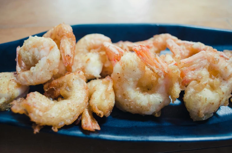 a blue plate topped with fried shrimp on top of a wooden table, by Carey Morris, unsplash, mingei, square, vanilla, 6 pack, battered