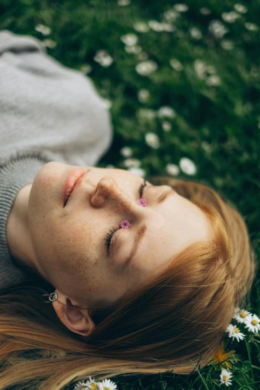 a woman laying in the grass with her eyes closed, inspired by Elsa Bleda, trending on pexels, renaissance, ginger hair with freckles, flower face, realistic person, smart looking