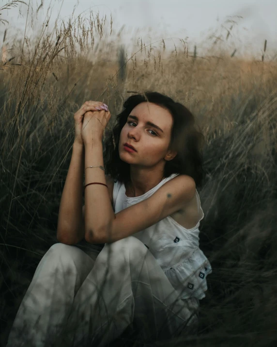 a woman sitting in a field of tall grass, inspired by Elsa Bleda, trending on pexels, with a hurt expression, non binary model, heartbroken, wearing white clothes