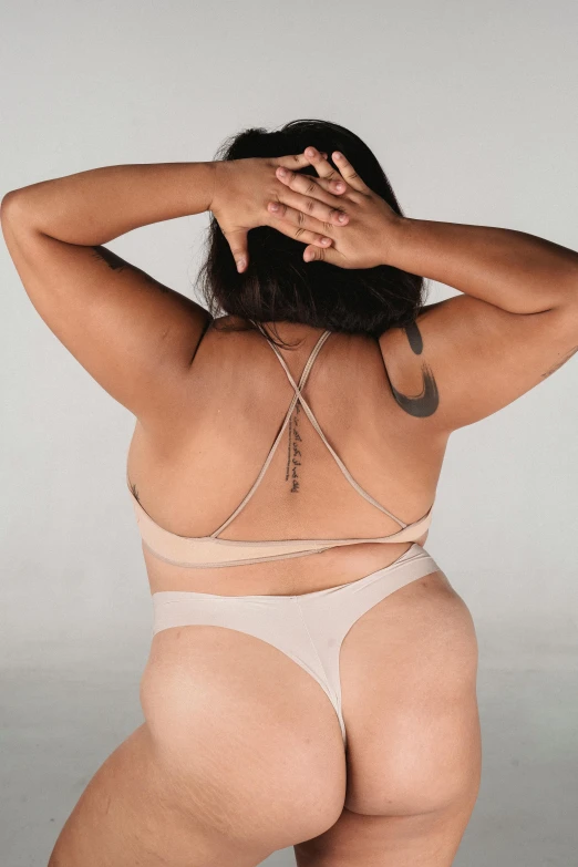a woman in a bikini with a tattoo on her back, by Jessie Alexandra Dick, trending on pexels, renaissance, muted colored bodysuit, plus size woman, set against a white background, wearing leotard