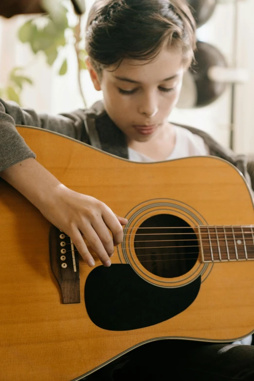 a young boy is playing an acoustic guitar, an album cover, by Everett Warner, pexels, australian, profile pic, at home, thumbnail