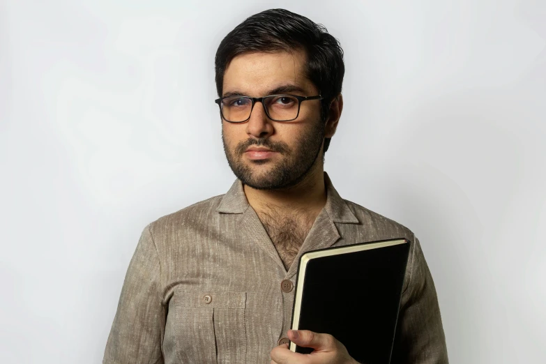 a man with glasses is holding a book, an album cover, inspired by Ismail Acar, studio portrait, holding notebook, reza afshar, anton fadeev 8 k