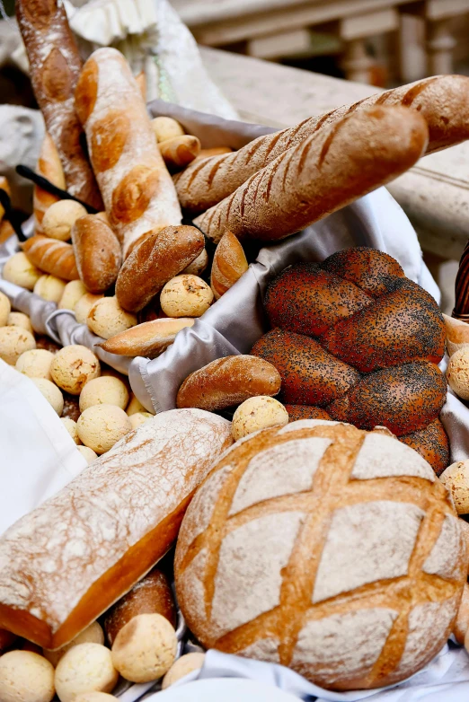 a table topped with lots of different types of bread, up-close, holding a baguette, market, up close