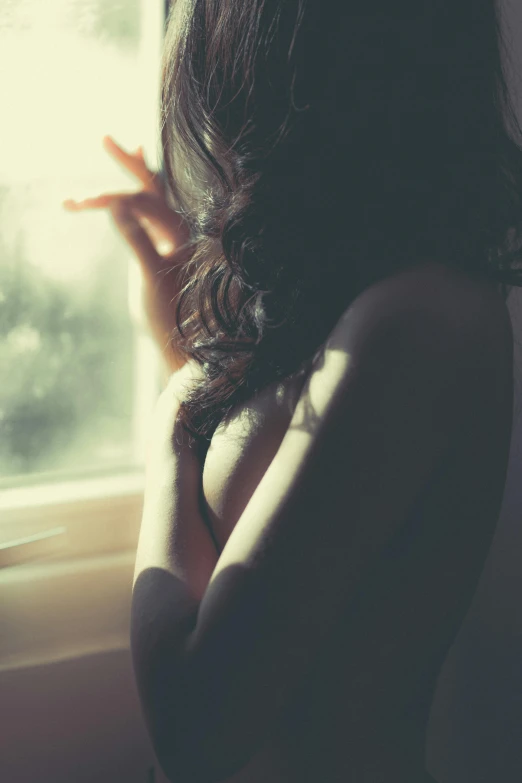 a woman smoking a cigarette in front of a window, a picture, inspired by Elsa Bleda, trending on pexels, romanticism, sun glare, hands behind back, curly dark hair, what depression looks like