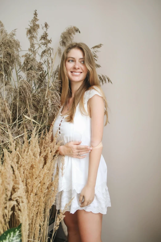 a beautiful young woman standing next to a tall plant, pexels contest winner, wearing a cute white dress, with long blond hair, gif, smiling