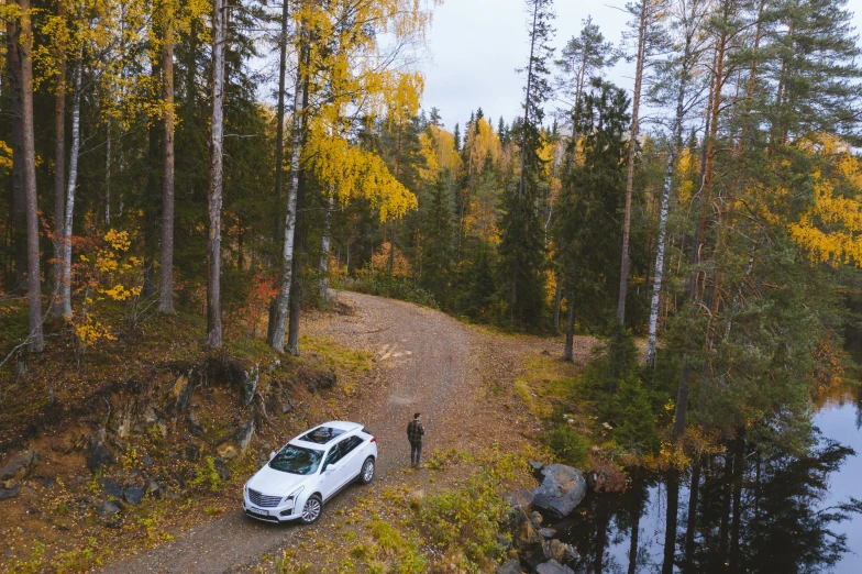 a white car parked on a dirt road next to a body of water, by Jaakko Mattila, pexels contest winner, hurufiyya, in the autumn forest, full body model, wide high angle view, campsites