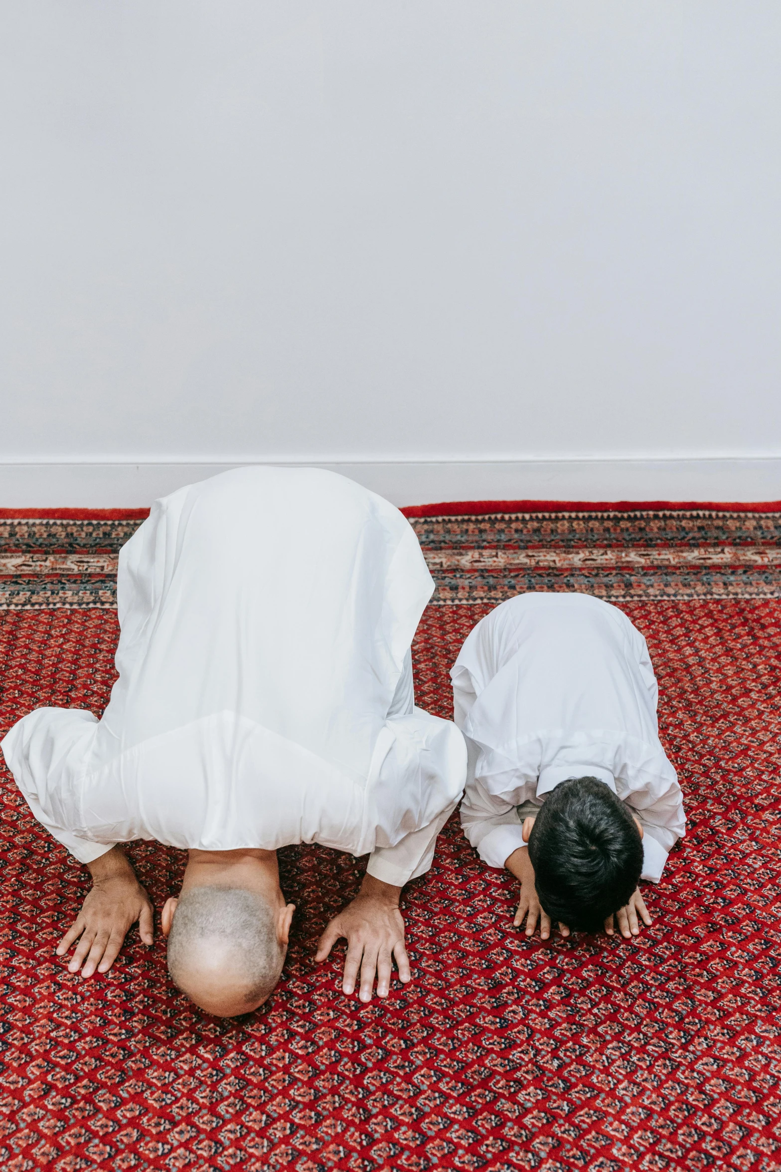 two men are doing a handstand on a rug, unsplash, hurufiyya, little boy wearing nun outfit, doing a prayer, - 9, head down