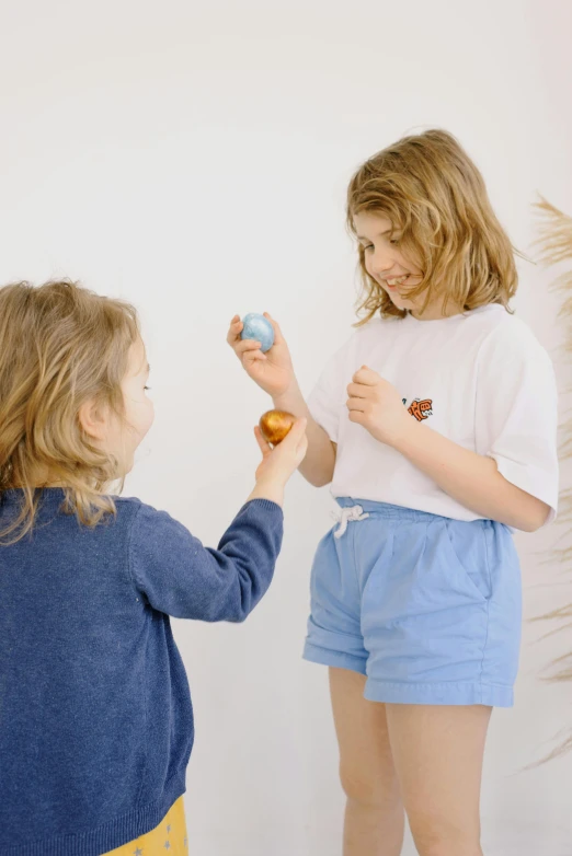 a couple of little girls standing next to each other, by Anita Malfatti, interactive art, holding easter eggs, wearing a light blue shirt, thumbnail, kids toy