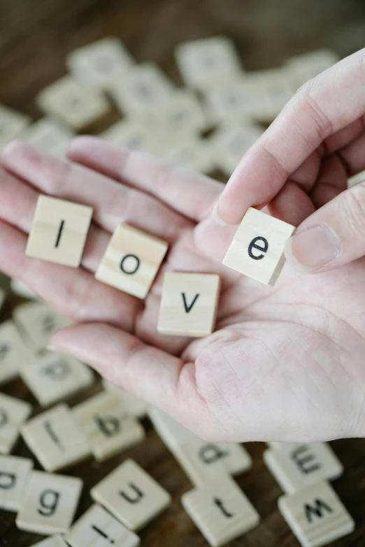 the word love spelled with scrabbles in a person's hand, by Arabella Rankin, square, high quality photo, a wooden, medium-shot