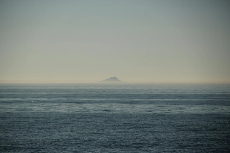a large body of water with a small island in the distance, a picture, unsplash, romanticism, view from the sea, very hazy, cornwall, chile