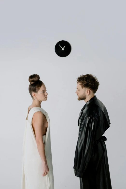 a man and a woman standing in front of a clock, an album cover, by Alexis Grimou, trending on pexels, antipodeans, topknot, at a fashion shoot, very minimalistic, robe. perfect faces