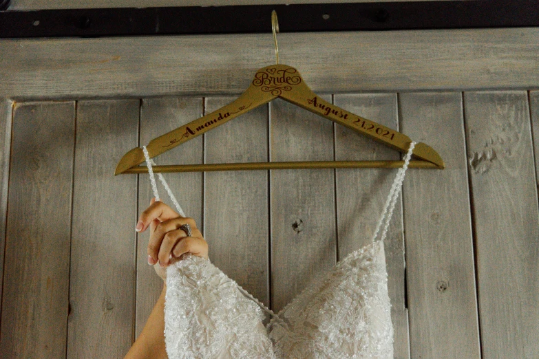 a close up of a person holding a dress on a hanger, inspired by Emma Ríos, rustic wood, with names, gold bra, woodstock