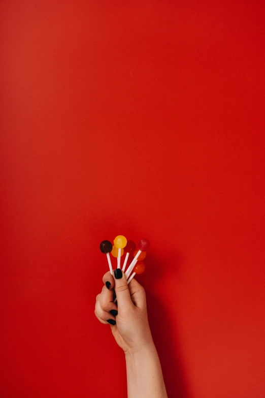 a hand holding a bunch of lollipop lollipop lollipop lollipop lollipop lollipop lollipop lo, by Andries Stock, pexels contest winner, pop art, red wall, flatlay, dark orange black white red, jen atkin