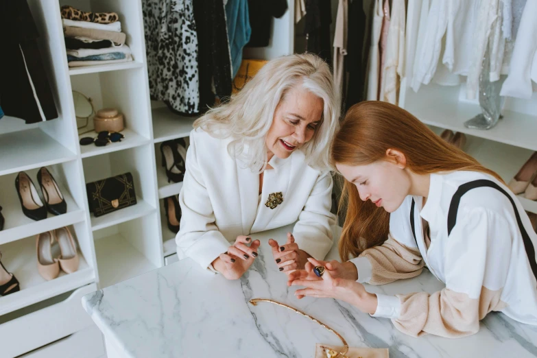 two women sitting at a table in a closet, trending on pexels, wearing an elegant outfit, old and young, at checkout, animated