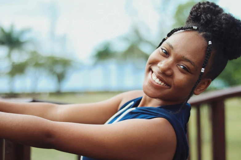 a woman smiles as she leans against a railing, pexels contest winner, black teenage girl, health supporter, avatar image, fit girl