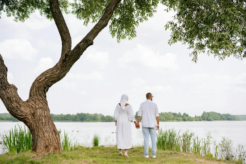 a man and a woman standing next to a tree, by Grytė Pintukaitė, pexels contest winner, hurufiyya, wearing white cloths, summer lake setting, walking to the right, picnic