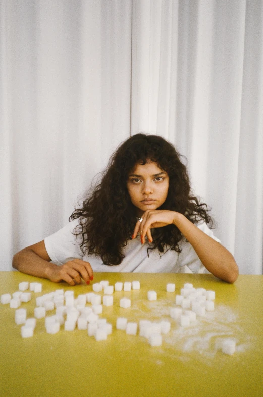 a woman sitting at a table with cubes of sugar, an album cover, curly dark hair, 2022 photograph, teen, nuri iyem