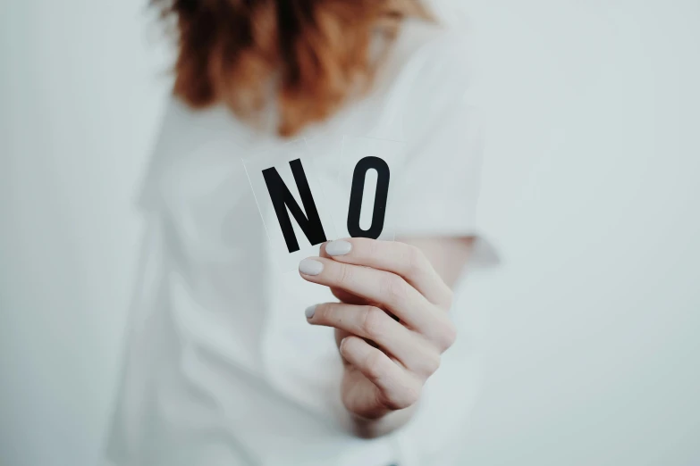 a woman holding a no sign in front of her face, by Arabella Rankin, trending on pexels, on a pale background, no two bodies, on a canva, unfocused