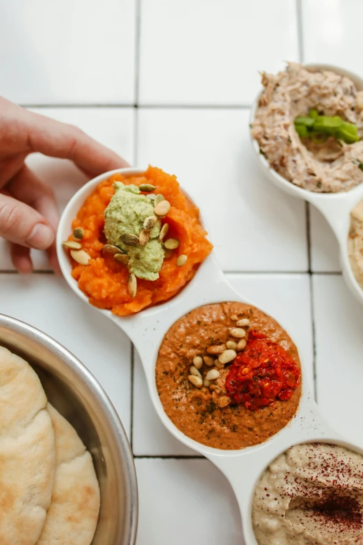 a table topped with bowls of different types of food, by Dan Content, trending on unsplash, dau-al-set, closeup of arms, humus, detailed product image, facing sideways