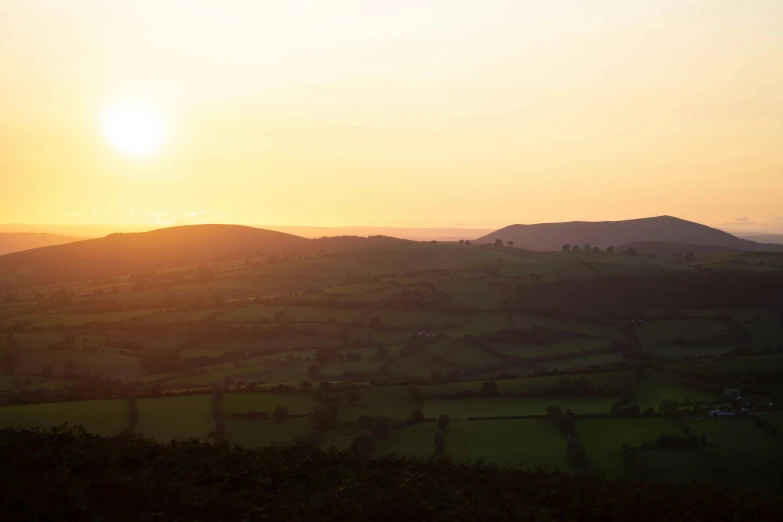 a couple of sheep standing on top of a lush green hillside, by Julian Allen, pexels contest winner, renaissance, sunset panorama, black mountains, pastel orange sunset, panoramic