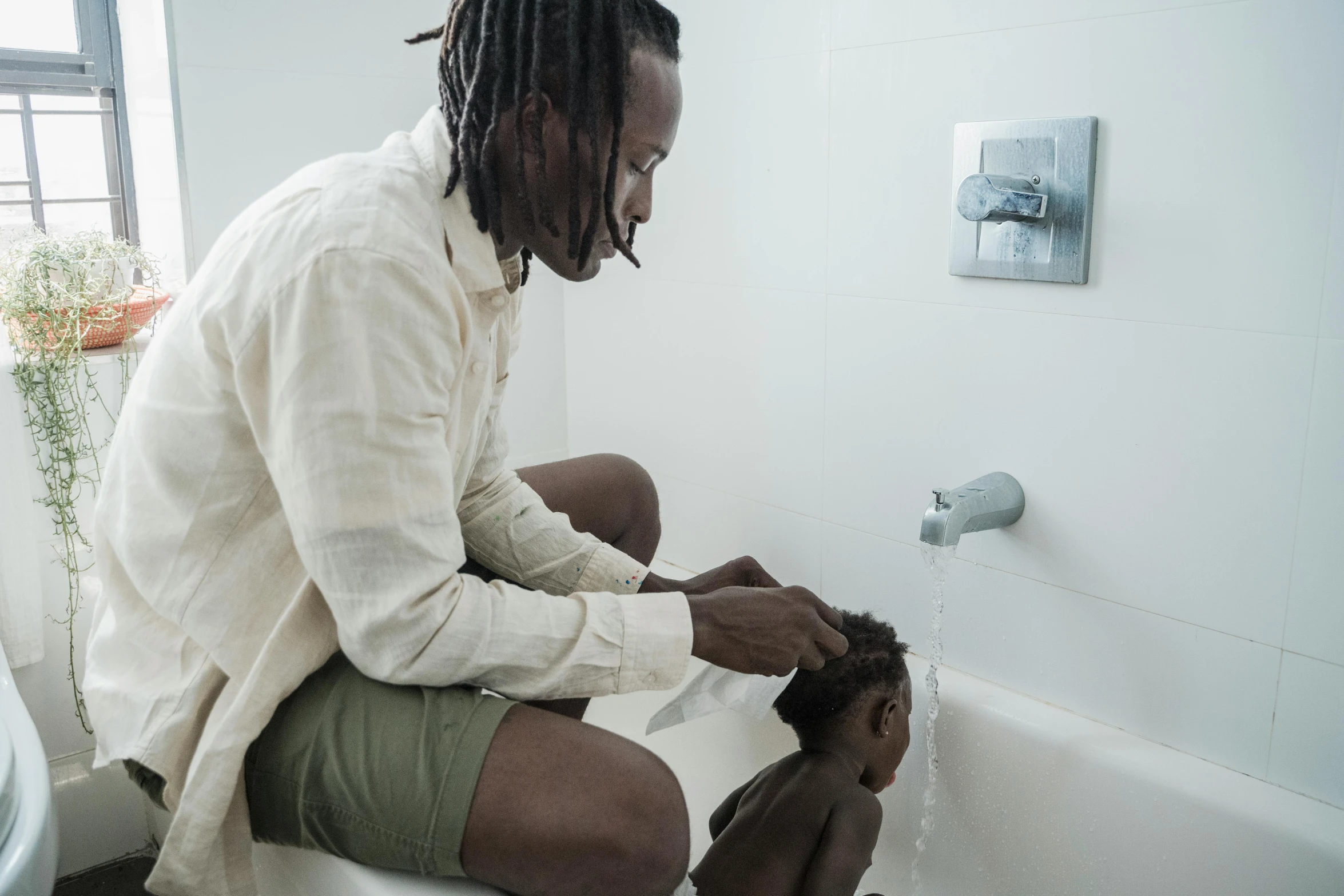 a man washing his hair in a bathtub, by Daniel Lieske, pexels contest winner, father with child, dreadlock black hair, african aaron paul, with grey skin