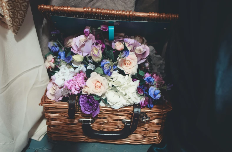 a wicker basket filled with lots of flowers, a colorized photo, unsplash, purple and blue leather, in suitcase, romantic undertones, a quaint