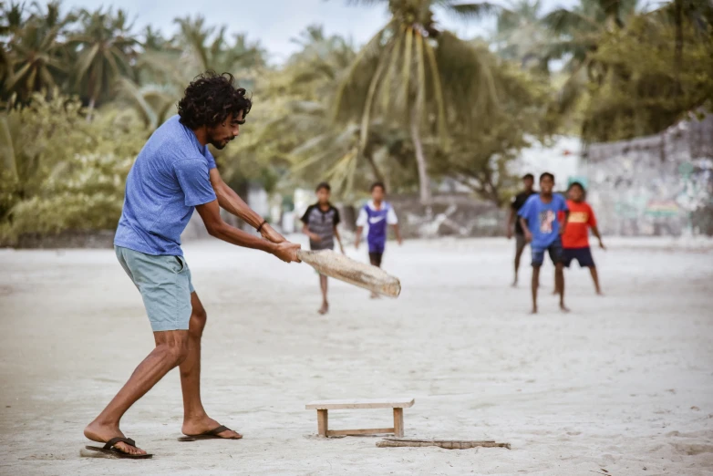 a man swinging a baseball bat at a ball, hurufiyya, in a beachfront environment, tribe members chasing, indigo, official